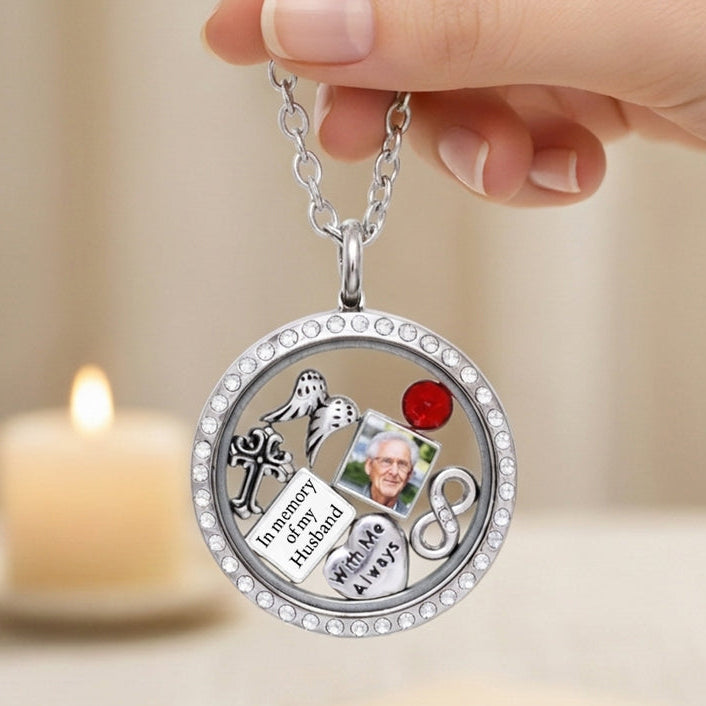 Round silver memorial locket pendant with picture charm, held by a hand with a blurred candle in the background.